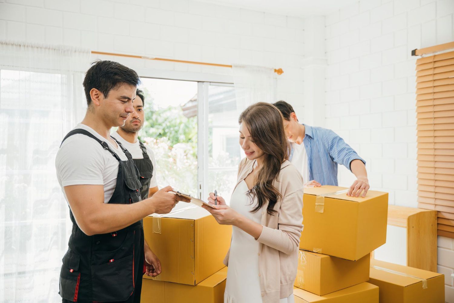Woman signing a document with movers. Cardboard boxes are stacked in a bright room.