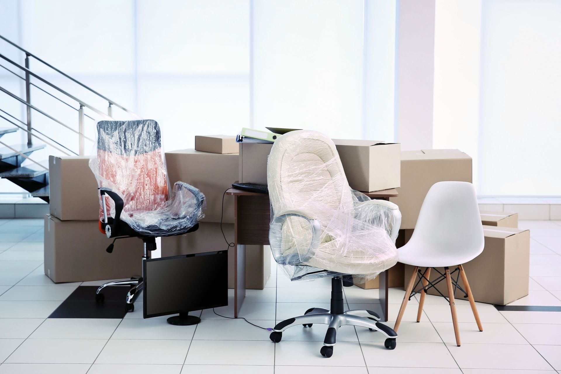 A room filled with boxes and office furniture wrapped in plastic.